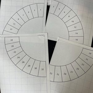 May include: Several white paper templates with a grid pattern and a semi-circular design are arranged on a surface. Each template is divided into numbered sections, ranging from 1 to 33, likely for a craft or design project.