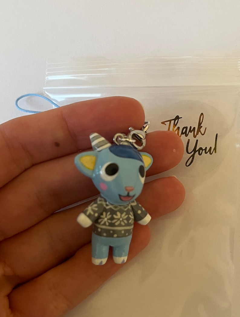 May include: A blue and white animal character keychain with a gray and white sweater. The keychain has a silver chain and a blue lanyard. The keychain is in a clear plastic bag with a sticker that says "Thank You".