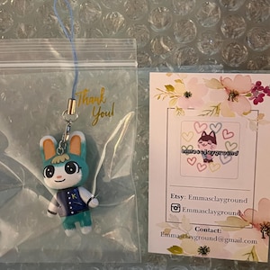 May include: A teal blue and white animal crossing character keychain with a blue jacket and a green hat. The character is holding a green sword. The keychain is in a clear plastic bag with a thank you note. The background is a white bubble wrap sheet.
