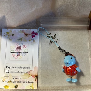 May include: A blue and red handmade polymer clay charm of a hippopotamus wearing a Hawaiian shirt. The charm is attached to a string and is packaged in a clear plastic bag with a thank you note.