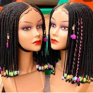 May include: Two mannequin heads with black braided wigs. The braids are adorned with colorful beads at the ends and decorative charms. One wig has pink accents. The mannequins have makeup with red lipstick.