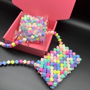 May include: A handmade, colorful beaded purse with a matching strap. The purse is made of small, square beads in pastel colors. A pink box contains more beads, wire, and tools for crafting. The purse is approximately 6 inches wide.