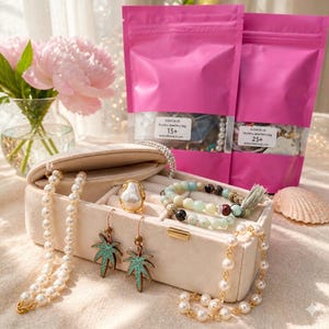 May include: A beige jewelry box filled with various jewelry pieces, including a pearl necklace, a gold ring with a pearl, and turquoise palm tree earrings. Two pink bags with the text "Mystery jewellery bag" are in the background.