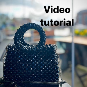 May include: A black beaded handbag with a silver chain strap. The bag has a round top handle and is made of small, round beads. The text "Video tutorial" is visible in the background.