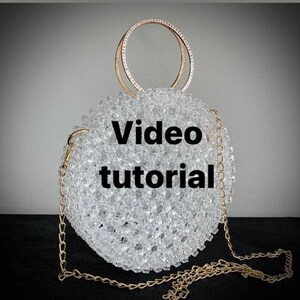 Peut inclure: Un sac à main en perles transparentes avec une chaîne dorée et des poignées circulaires dorées. Le sac est rond et recouvert de petites perles transparentes. Le texte "Video tutorial" est affiché sur le sac.