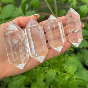 May include: Four clear, double-terminated quartz crystal points of varying sizes. Each crystal features a hexagonal prism shape with pointed terminations at both ends, displaying natural internal inclusions and a transparent, glass-like appearance.