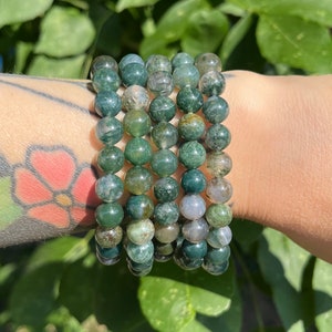 May include: A stack of green agate bead bracelets. The beads are round and have a mottled green and white pattern.