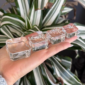 May include: Four clear glass square display stands of varying sizes. The stands are made of thick glass and have a polished finish.