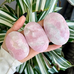May include: Three pink and white oval-shaped polished stones. The stones have a smooth, polished surface and a natural, organic shape.