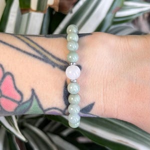May include: A green jade stone bracelet with a single white stone bead in the center.