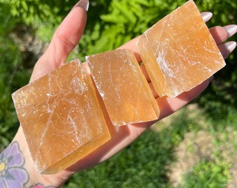 Può includere: Tre cubi di cristallo di selenite arancione traslucidi. I cristalli sono lisci e hanno un aspetto naturale e grezzo.