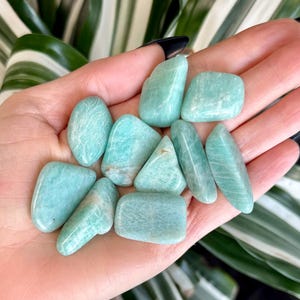 May include: A collection of smooth, light green tumbled Amazonite stones. The stones are various shapes and sizes, and have a natural, polished finish.