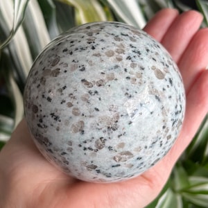 May include: A white and grey speckled sphere, a polished stone orb, with a smooth, rounded surface.