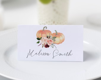 May include: A white place card with a watercolor illustration of two pumpkins and flowers. The text "Melissa Smith" is written in black cursive.