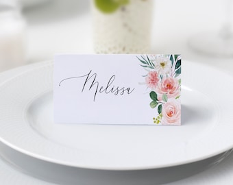 May include: A white place card with the name "Melissa" written in black cursive script. The card is decorated with a watercolor floral design featuring pink and white flowers and green leaves.