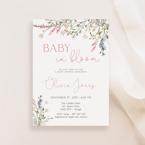 Pu&ograve; includere: Invito per baby shower con elementi floreali. L'invito presenta il testo "BABY in bloom" in una scrittura delicata, insieme al nome "Olivia Jones" e ai dettagli dell'evento. Illustrazioni floreali in rosa, blu e verde adornano la parte superiore e inferiore.