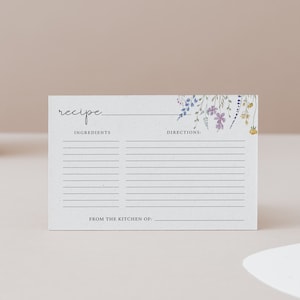 Puede incluir: Una tarjeta de receta en blanco con un dise&ntilde;o floral en tonos de morado, azul y amarillo. La tarjeta tiene l&iacute;neas para escribir los ingredientes y las instrucciones. El texto "receta" est&aacute; en la parte superior de la tarjeta. El texto "De la cocina de:" est&aacute; en la parte inferior de la tarjeta.
