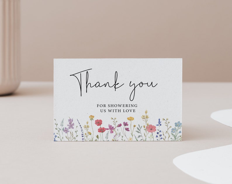 Puede incluir: Tarjeta de agradecimiento con borde floral. La tarjeta es blanca con texto negro que dice "Gracias por colmarnos de amor".