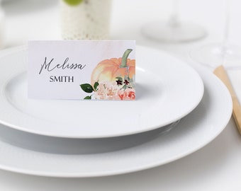 May include: A white place card with the name "Melissa SMITH" written in black cursive script. A watercolor illustration of a pumpkin with pink and orange flowers is on the right side of the card.
