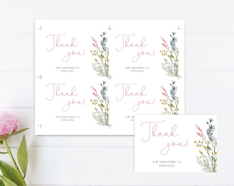 May include: White thank you cards with floral watercolor illustrations. The cards feature the text "Thank you! For showering us with love" in a delicate pink script. The floral design includes blue, pink, and yellow wildflowers.