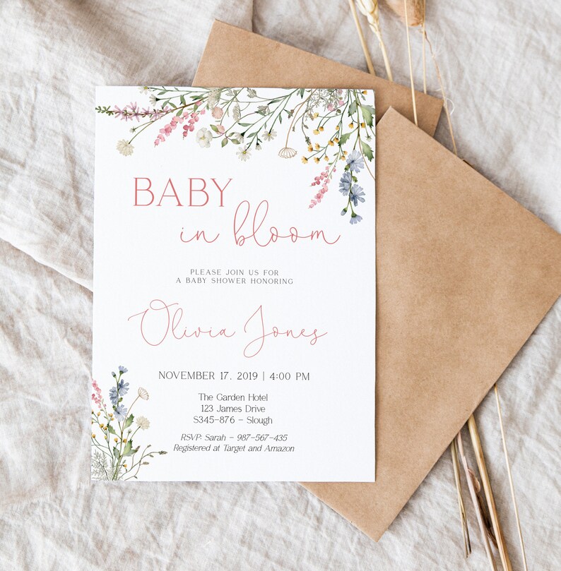 Pu&ograve; includere: Invito per baby shower con decorazioni floreali. L'invito recita "BABY in bloom" in un delicato carattere corsivo, con il nome "Olivia Jones" sotto. Sono inclusi anche data, ora, luogo e informazioni RSVP. L'invito &egrave; accompagnato da una busta marrone.