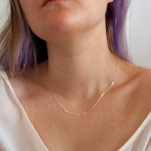 May include: A delicate silver chain necklace with a simple design. The chain is thin and has a subtle shimmer.