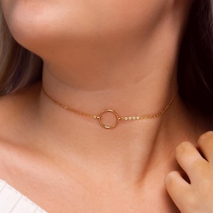 May include: A gold choker necklace with a simple circle pendant.