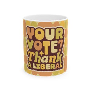 May include: A white ceramic mug with a retro design. The mug features the text "YOUR VOTE? Thank A LIBERAL" in brown, yellow, and orange colors. The background has a repeating pattern of yellow and orange circles.