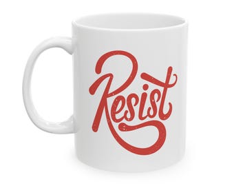 May include: White ceramic mug with a red handwritten word "Resist" on the front.