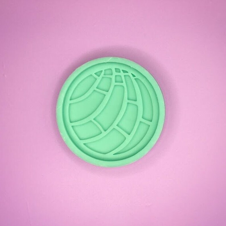 May include: A green silicone mould shaped like a traditional Mexican sweet bread, known as a concha.