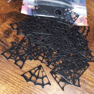 May include: A bag of black spiderweb confetti, perfect for Halloween decorations. The confetti is made of thin, black paper and is shaped like spiderwebs.