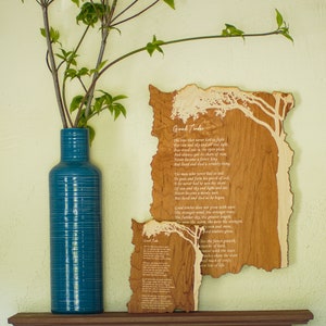May include: A teal blue vase with a textured surface holds green leafy branches. Two wooden plaques with a tree design and the poem "Good Timber" are displayed on the wall. The plaques are made of light brown wood.