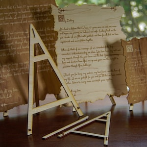 May include: Three wooden display stands for scrolls or other paper items. The stands are made of light brown wood and have a triangular shape. The stands are on a wooden surface.