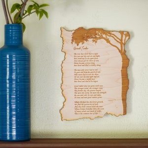 May include: A blue ceramic vase with a textured surface holds green leafy branches. To the right, a wooden plaque with the poem "Good Timber" is displayed. The plaque has a tree design and a burnt edge.