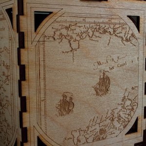 Peut inclure: Une boîte en bois avec une carte d'une côte et le texte "M.A.R.E.  het Caniel" gravé sur le devant.