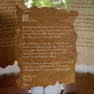 May include: A wooden scroll with a handwritten message about marriage and love. The scroll is on a wooden stand and the text reads "It's hard to believe that it's been 10 years since we said our vows and began our journey as husband and wife. Looking back on the past decade, I am filled with gratitude and love for all that we have experienced and accomplished together. When I think of our marriage, I am reminded of the deep connection and understanding we share. You have been my rock and my support, through the good times and the bad. Your unwavering love and devotion have lifted me up and given me the strength to persevere through life's challenges. Thank you for being my partner, my best friend, and the love of my life. I am so grateful for you and for all that we have created together. Here's to many more wonderful years together. With all my love, Wad's Lab."