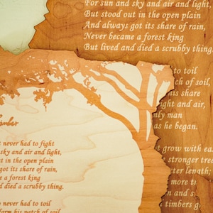 May include: Wooden artwork with a layered design featuring a tree silhouette and the words "Good Timber" and a poem. The artwork is primarily brown with lighter wood accents and a light green background.