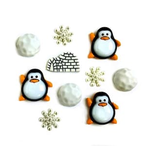 May include: A set of 10 penguin and winter-themed buttons. The buttons are white, black, and orange. There are two penguins, two snowballs, an igloo, and four snowflakes.
