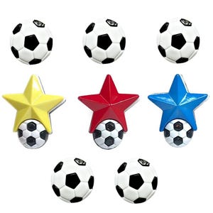 May include: An assortment of soccer ball-themed decorative items. The image features several white and black soccer balls, along with star-shaped embellishments in yellow, red, and blue, each also paired with a soccer ball.