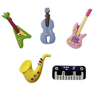 May include: Five colorful plastic musical instrument buttons: a green electric guitar, a blue violin, a pink electric guitar, a yellow saxophone, and a black and white keyboard.