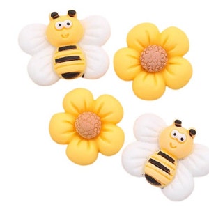May include: Four yellow and white fondant decorations, two are bees with black stripes and two are flowers with brown centers.