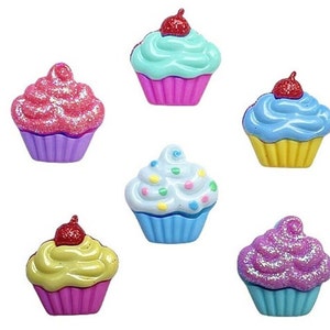 May include: Six colorful cupcake buttons with glitter and frosting details. The cupcakes are in various colors, including pink, blue, and yellow.