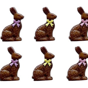 May include: Six chocolate bunny figurines with bows. The bunnies are brown and sitting upright. Three bunnies have pink bows and three bunnies have yellow bows.