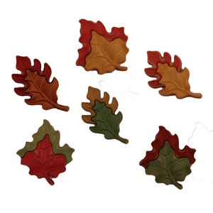 May include: Six wooden fall leaves in various shades of red, orange, green, and brown. The leaves are layered on top of each other, creating a three-dimensional effect.