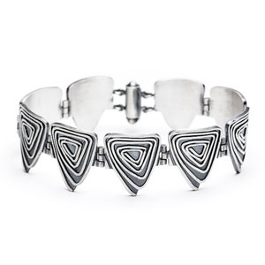 May include: A silver bracelet with a geometric design featuring a series of interlocking triangles with a swirling pattern.