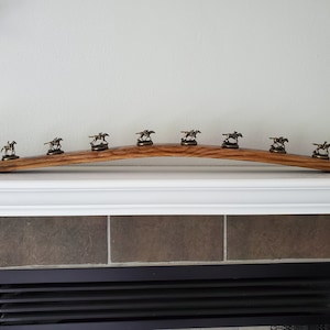 May include: A wooden wine barrel stave with a curved shape, decorated with eight small bronze horse figurines. The stave is displayed on a white mantel above a fireplace.