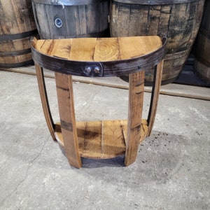 May include: A half-round wooden table with a metal band around the top and a shelf underneath. The table is made from reclaimed wood barrels.