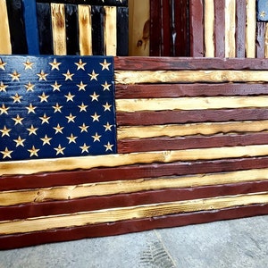 May include: A wooden American flag with red, white, and blue stripes. The flag is made of individual wood planks and has a distressed, rustic look.
