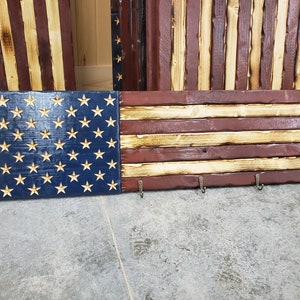 May include: A wooden American flag key rack with three hooks. The flag is painted in red, white, and blue with a distressed look. The stars are carved into the wood.