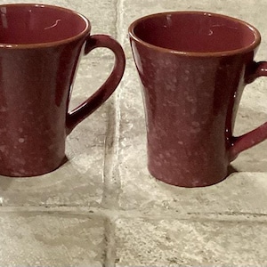 May include: Four burgundy ceramic mugs with speckled glaze and rounded handles.
